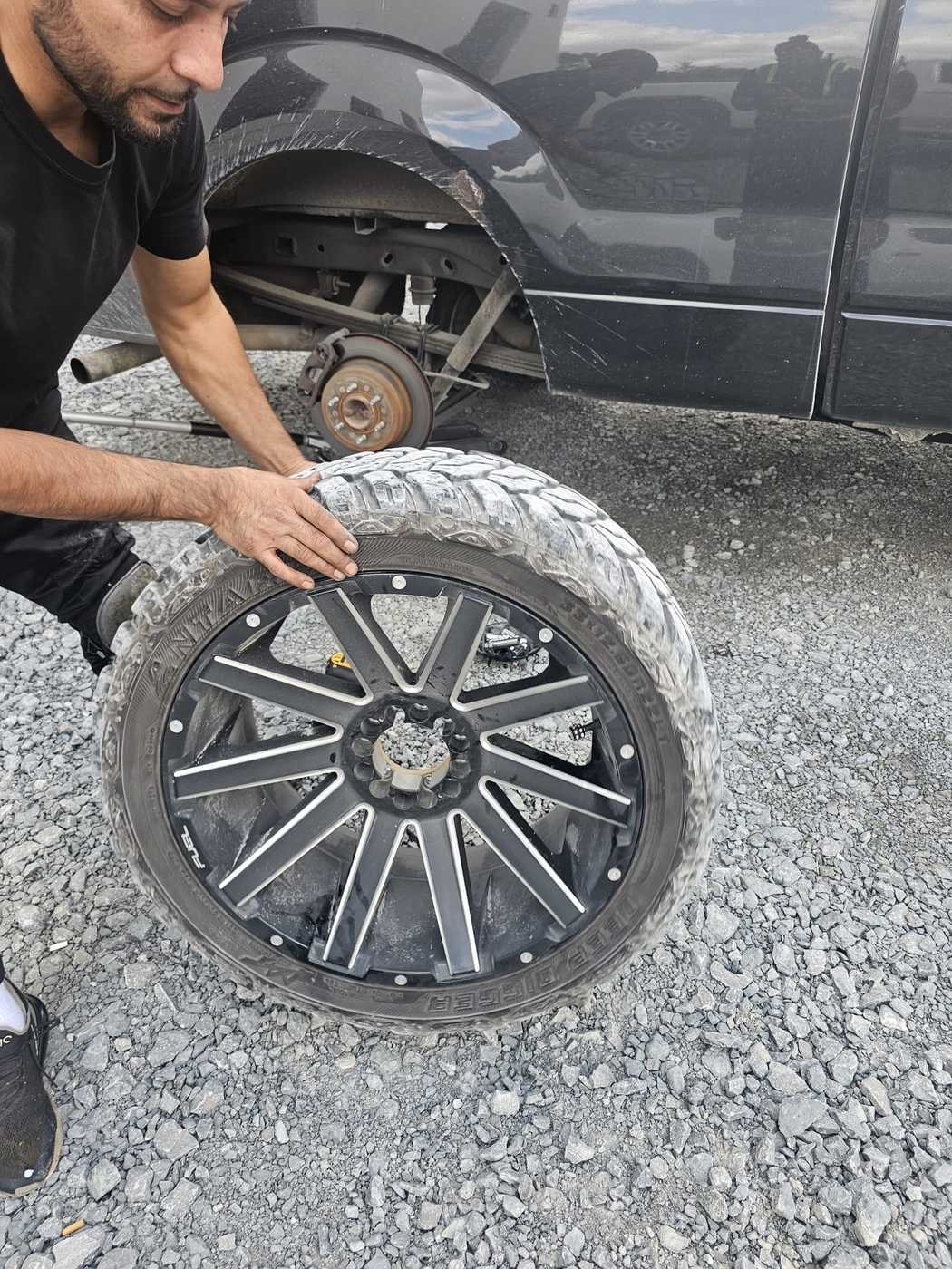 Owner mounting a large off-road tire on a customer's pickup truck on site